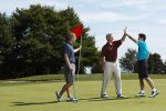 Three male golfers on green, one holds the flag, other two high-five